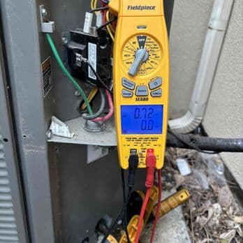 Technician using a Fieldpiece meter to diagnose an outdoor unit's electrical components